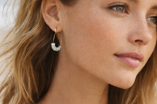 Close-up of a woman wearing gold hoop earrings with a neutral background